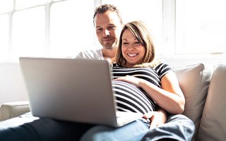 Schwangeres Paar mit Notebook auf Sofa